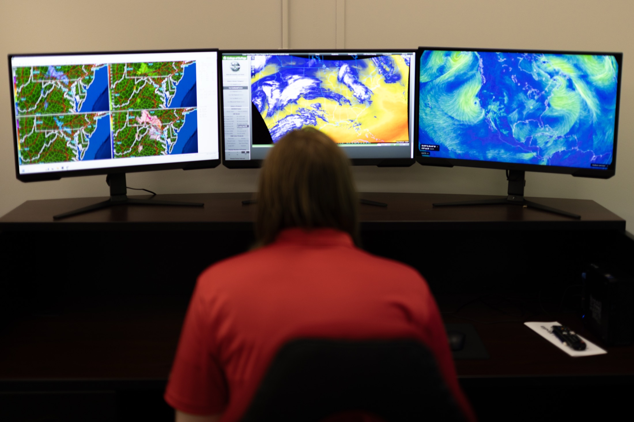 A DSOC forecaster monitoring radar, satellite water vapor, and wind-flow models across three displays